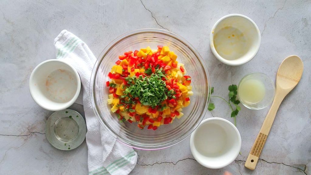 Cilantro on top of bell pepper mango pineapple salsa in a clear bowl