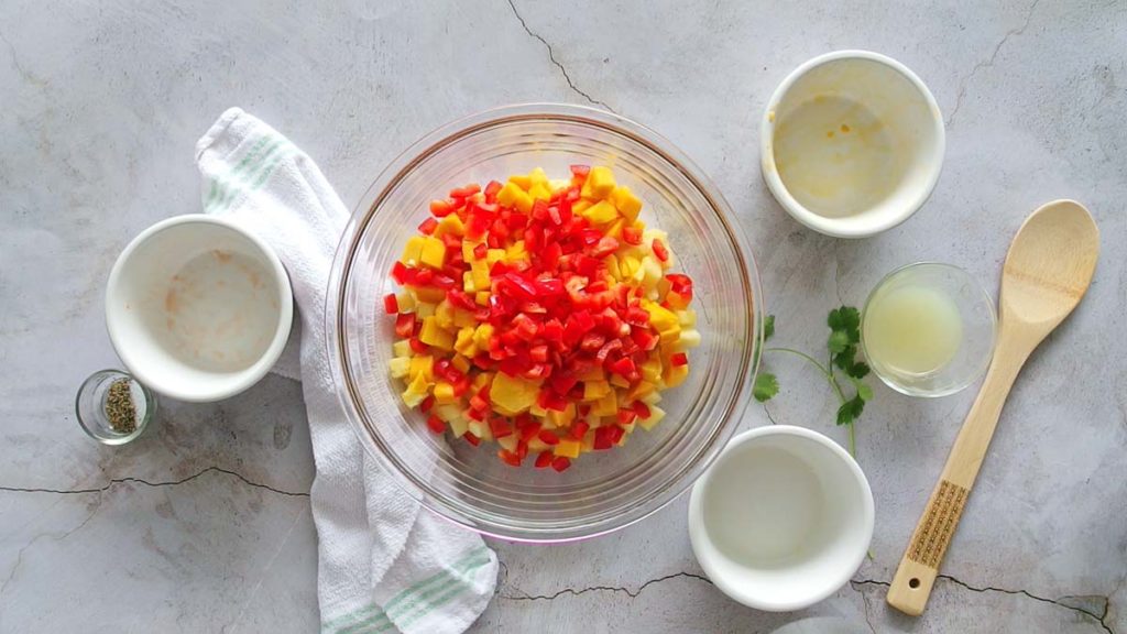 adding cilantro to pineapple mango salsa and mixing in a clear bowl