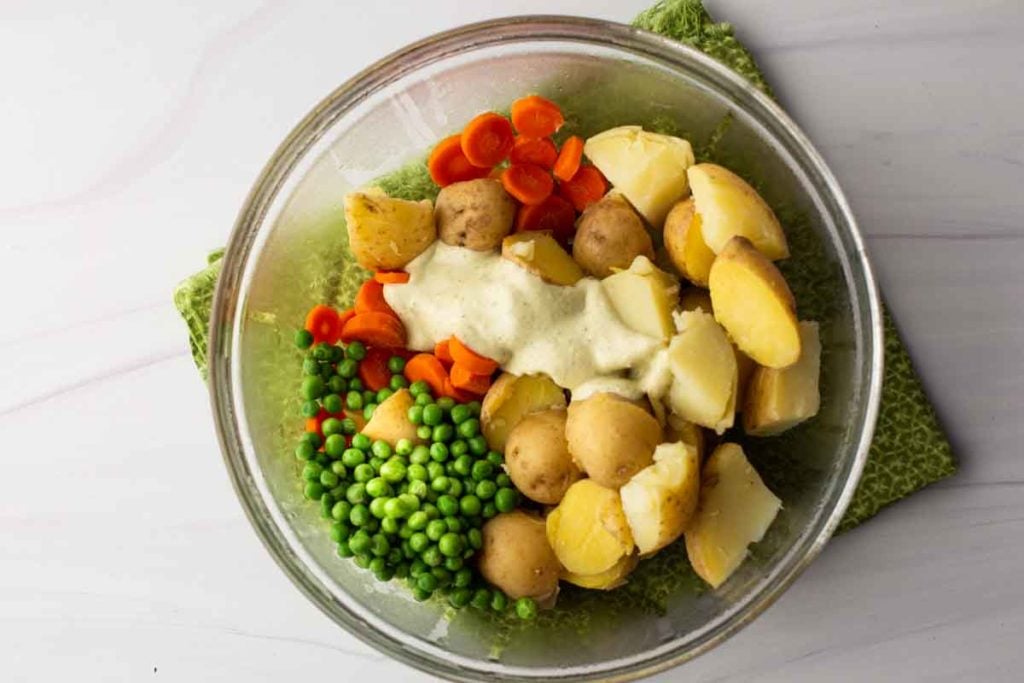 Mixing avocado cream sauce with potatoes, carrots and green peas to make avocado potato salad