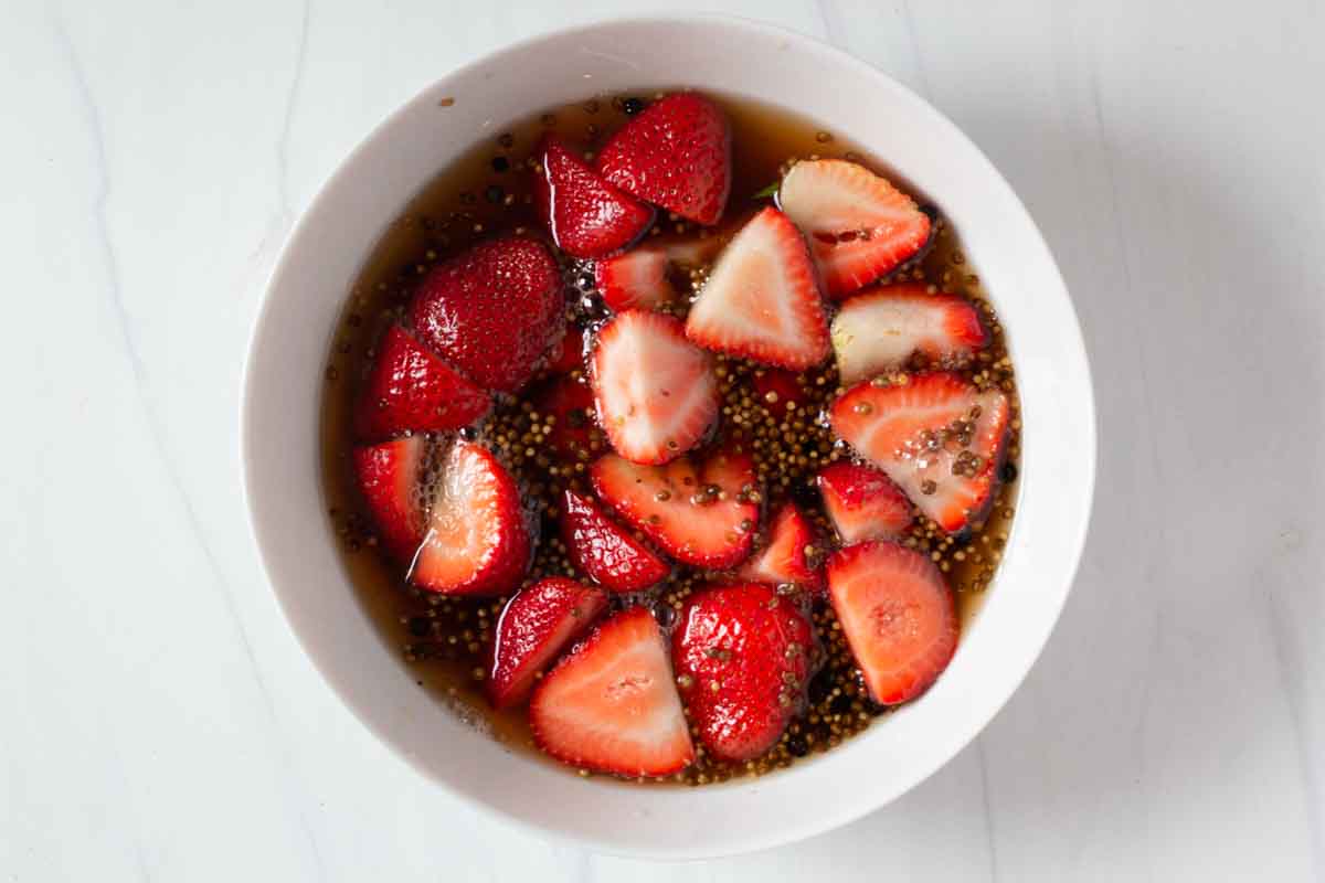 Sliced strawberries in pickling brine in a shallow white bowl