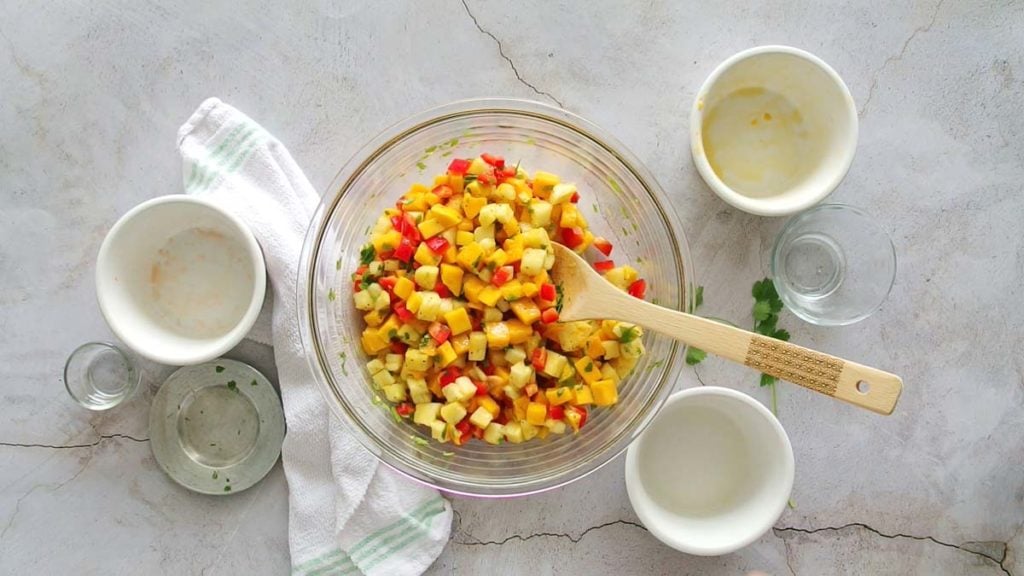 Pineapple Mango Salsa in a clear bowl with wooden spoon