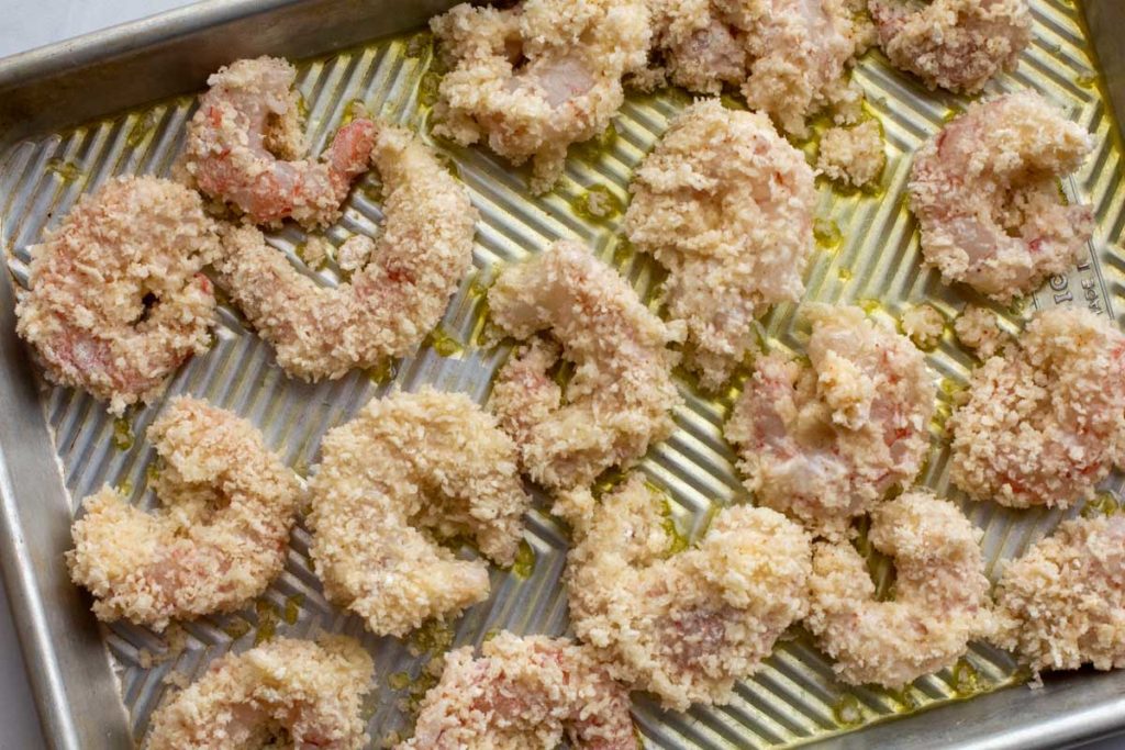 panko breaded shrimp on a sheet pan that's been coated with olive oil