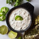 jalapeno aioli in a black bowl with cilantro, fresh limes and jalapeno