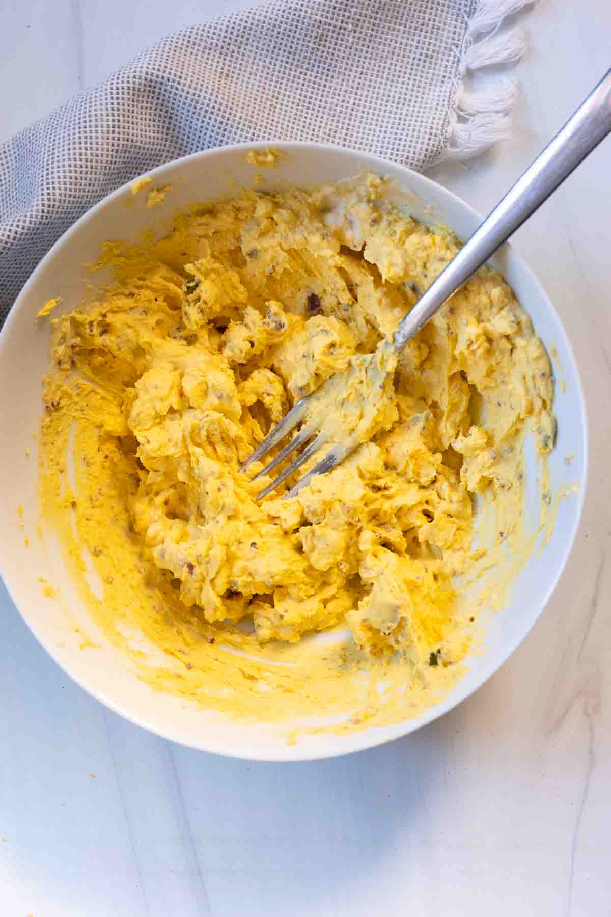 Using a fork to mix ingredients to make Bacon and Jalapeno deviled eggs.