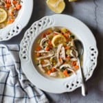 A bowl of chicken noodle soup with seasonings.