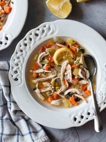 A bowl of chicken noodle soup with seasonings.