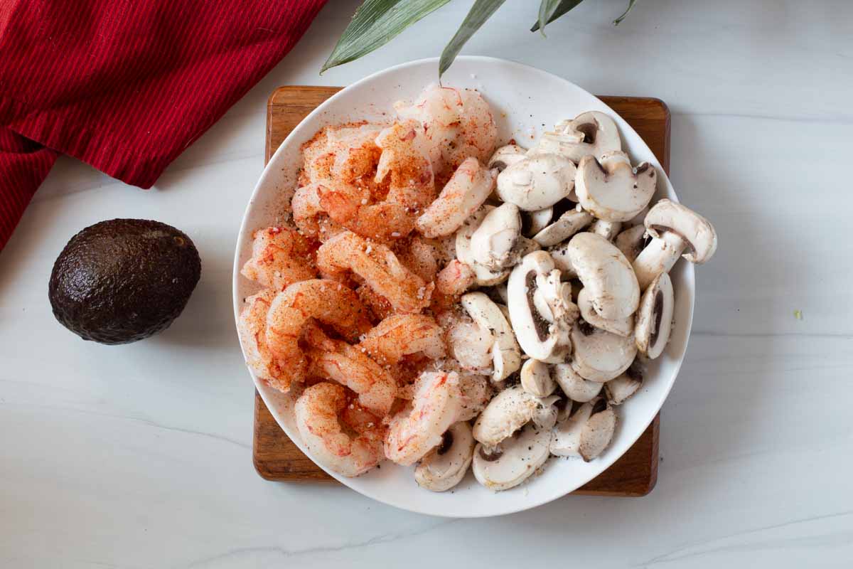 Shrimp and sliced mushrooms on a plate and seasoned to make Mexican Shrimp Tacos.