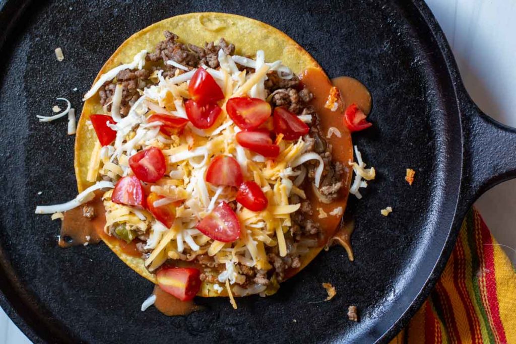 adding cheese and tomatoes to corn tortillas to make stacked enchiladas