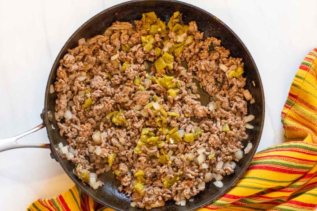 Browning beef onions and green chile peppers to make stacked enchiladas