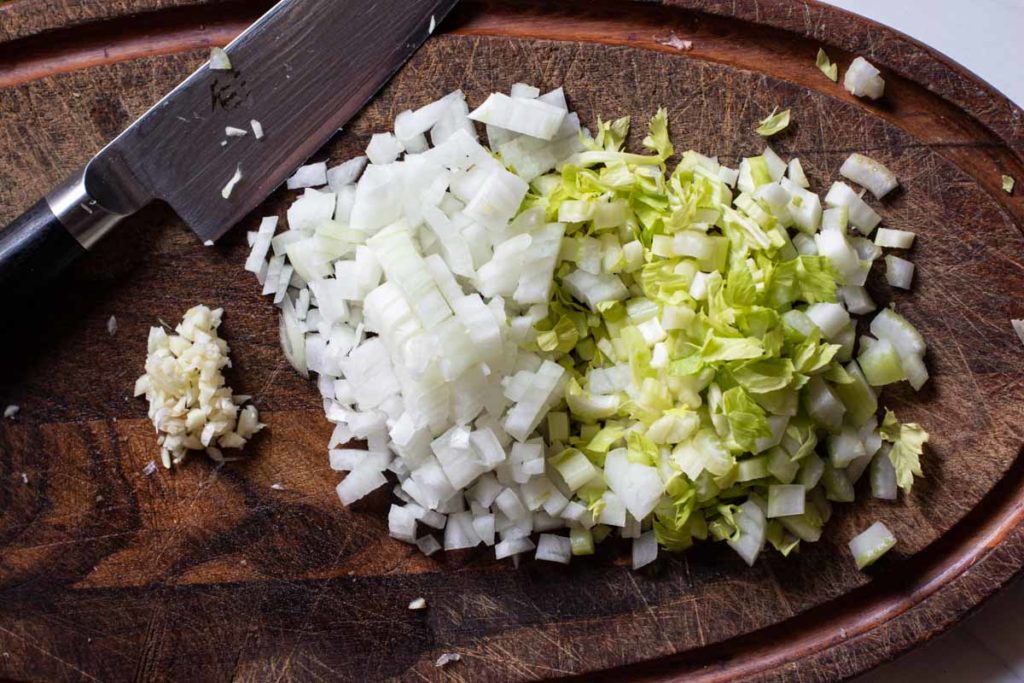 chopped celery, onions and garlic on a wood cutting board