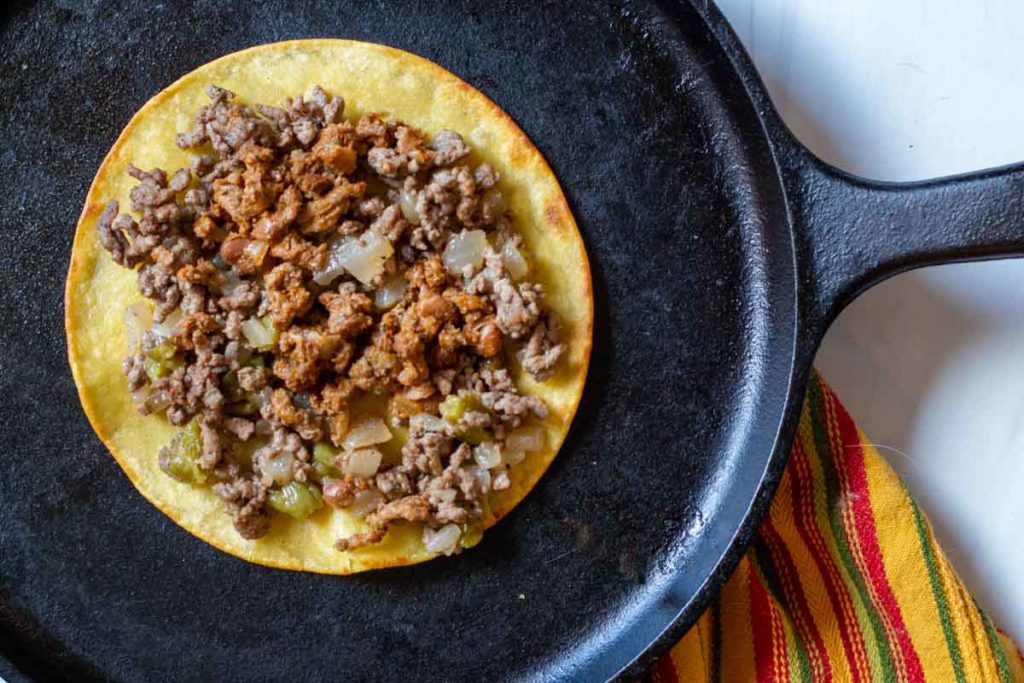 Placing ground beef on corn tortilla to make stacked enchiladas.