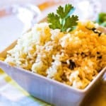 Oven baked rice in a white serving bowl garnished with parsley.