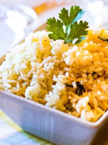 Oven baked rice in a white serving bowl garnished with parsley.