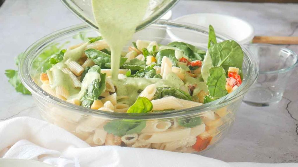 Adding dressing to penne pasta salad.