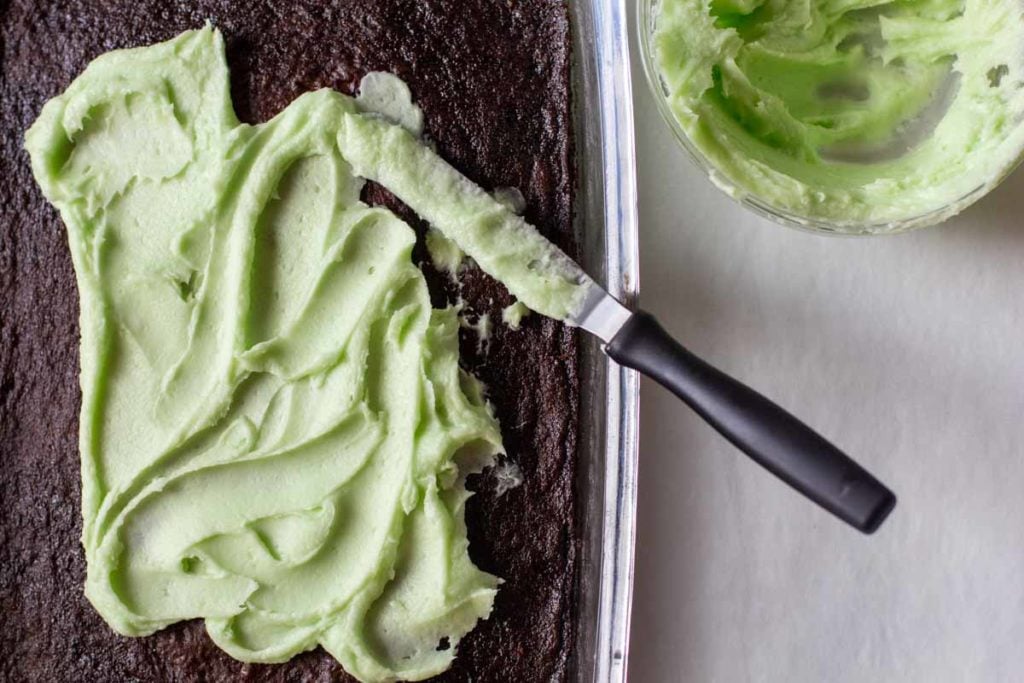 Frosting chocolate brownies with mint green frosting using an offset spatula.