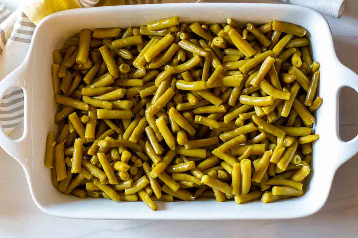 Placing canned beans in a casserole dish to make green beans with brown sugar and bacon.