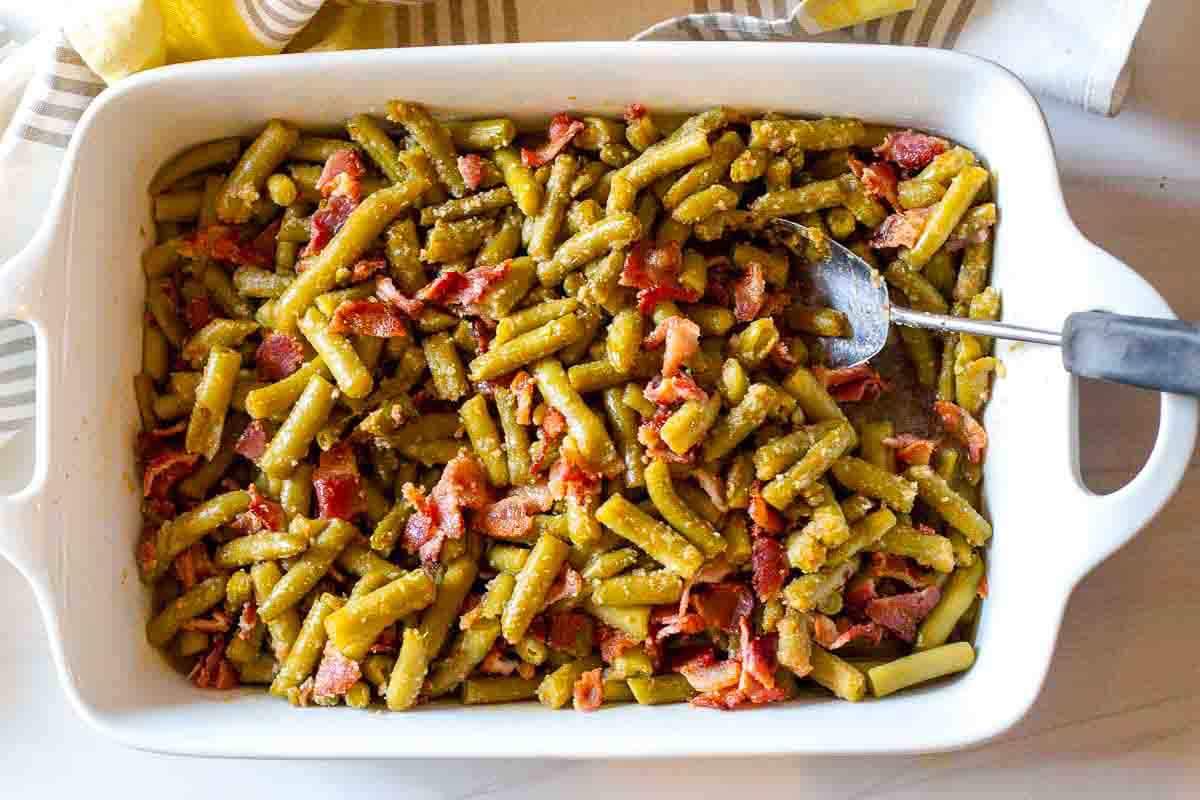 Adding cooked bacon to green bean casserole with brown sugar.