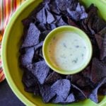 White queso dip served in a Fiesta Ware Green chips and dip plate with blue corn tornillas