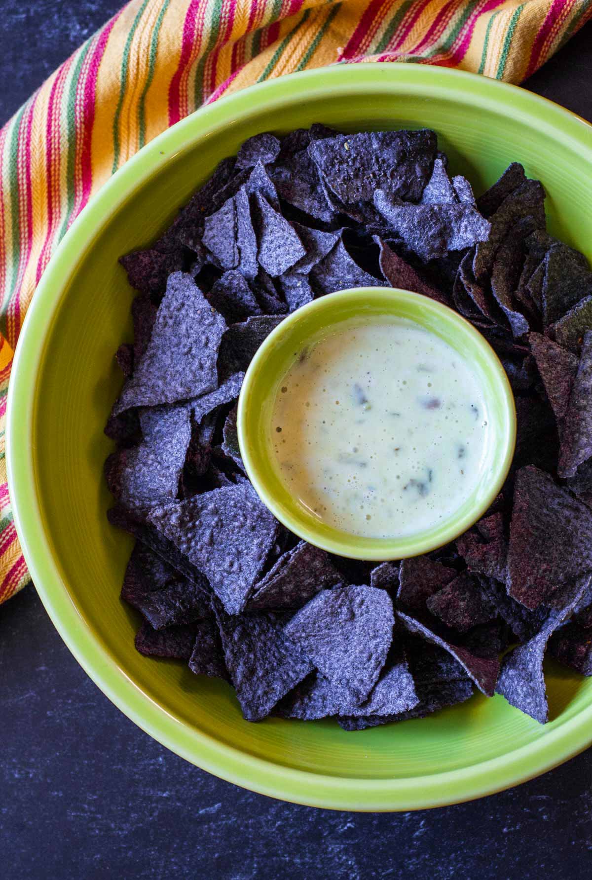 White queso dip served in a Fiesta Ware Green chips and dip plate with blue corn tornillas.