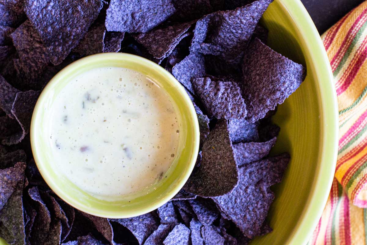 White queso dip recipe served in a green bowl with blue corn tortilla chips