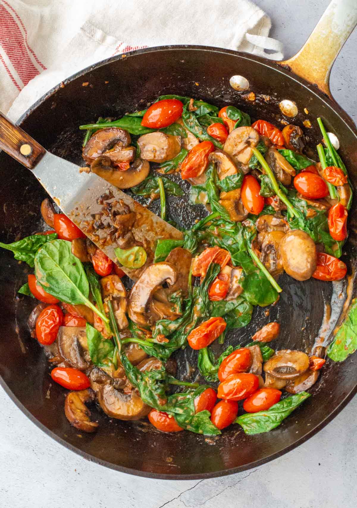 Adding spinach to a fry pan with cherry tomatoes and mushrooms to make chicken mushroom and spinach skillet dinner.