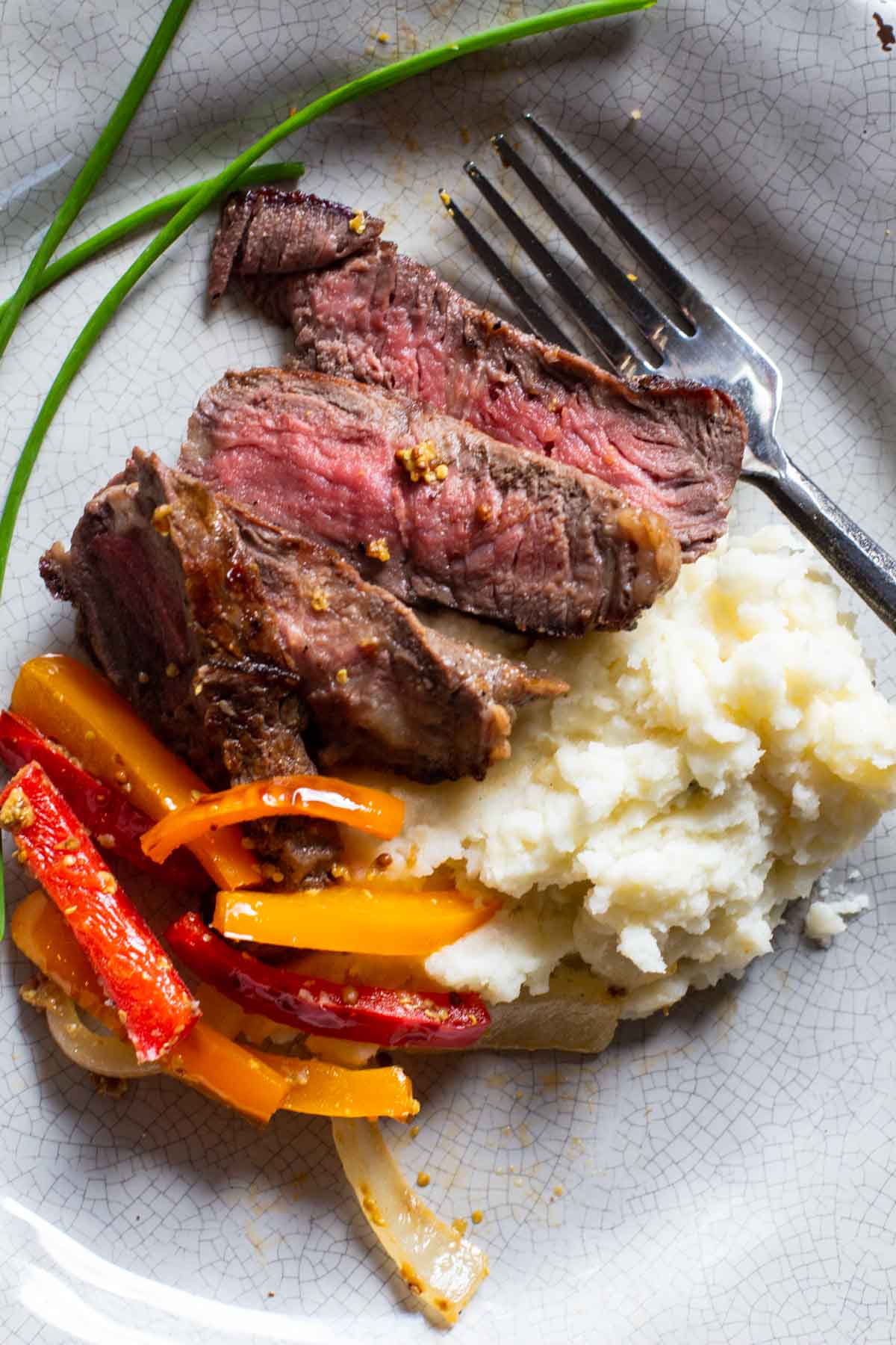 Bison steak recipe served with mashed potatoes and sauteed red and orange bell peppers.