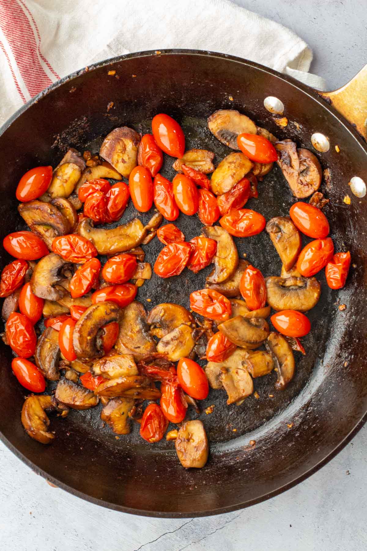 Cooking cherry tomatoes and mushrooms in a heavy skillet.