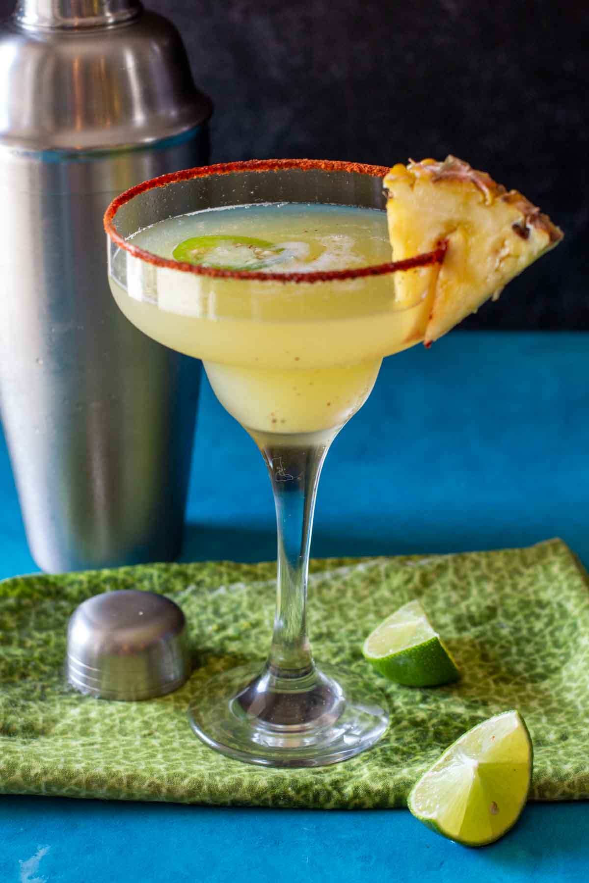 Spicy pineapple margarita garnished with a wedge of pineapple and rimmed with Tajin seasoning.