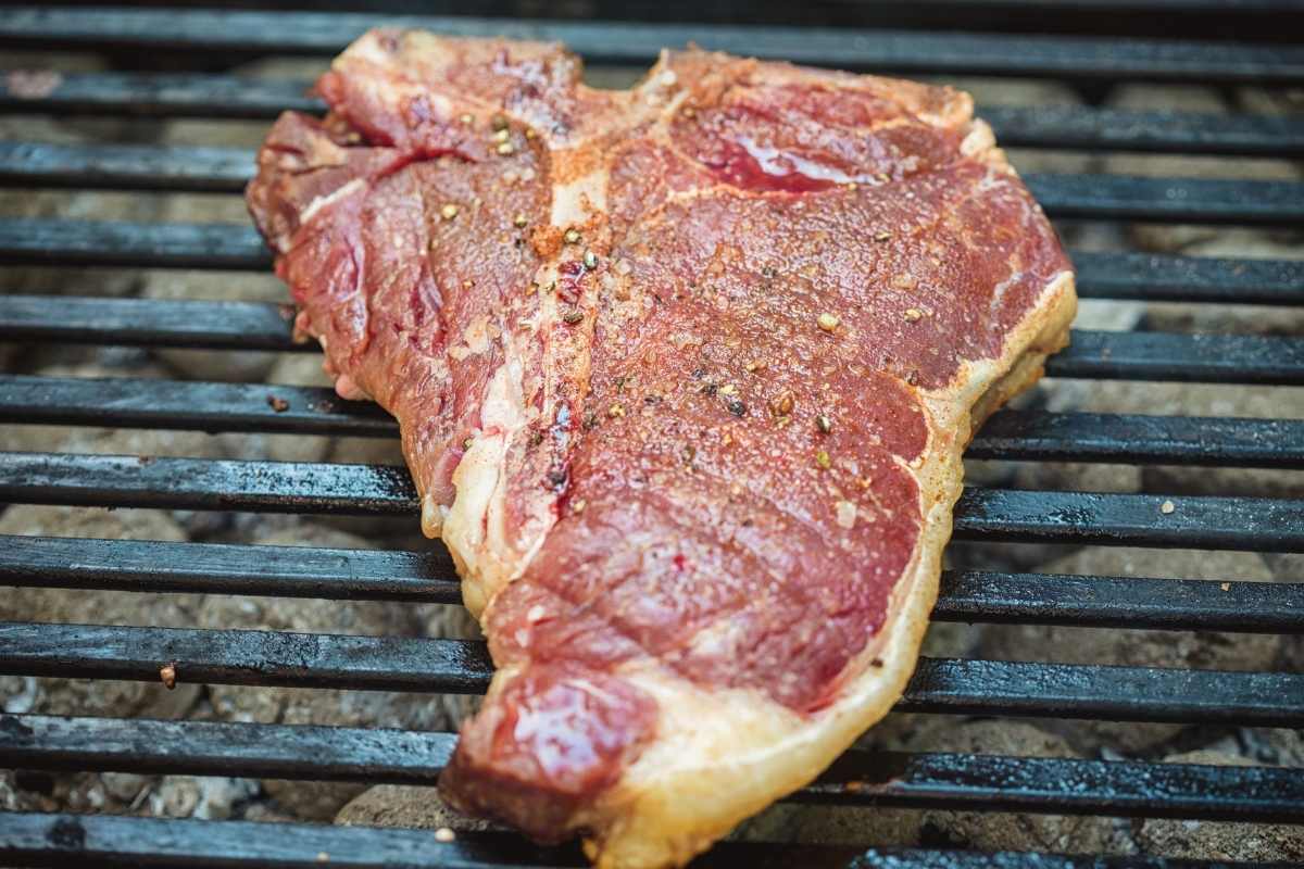 A t-bone steak cooking on the grill.