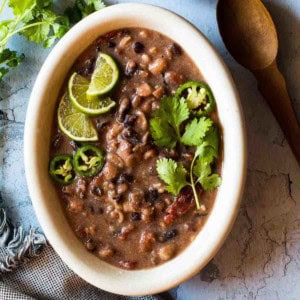 A bowl of slow cooker cowboy beans garnished with cilantro and limes.