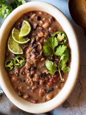A bowl of slow cooker cowboy beans garnished with cilantro and limes.
