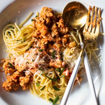 Chicken bolognese served on a pasta plate topped with parmesan cheese.