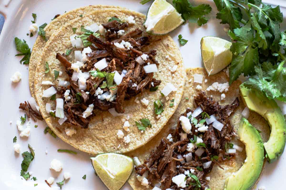 Slow cooker Beef Barbacoa Tacos with lime, cotija cheese and avocado.