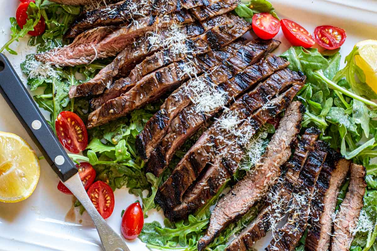 Steak Tagliata served on a bed of arugula greens with cherry tomatoes.