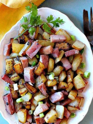 Fried ham and potaotes (country potatoes) on a white platter.