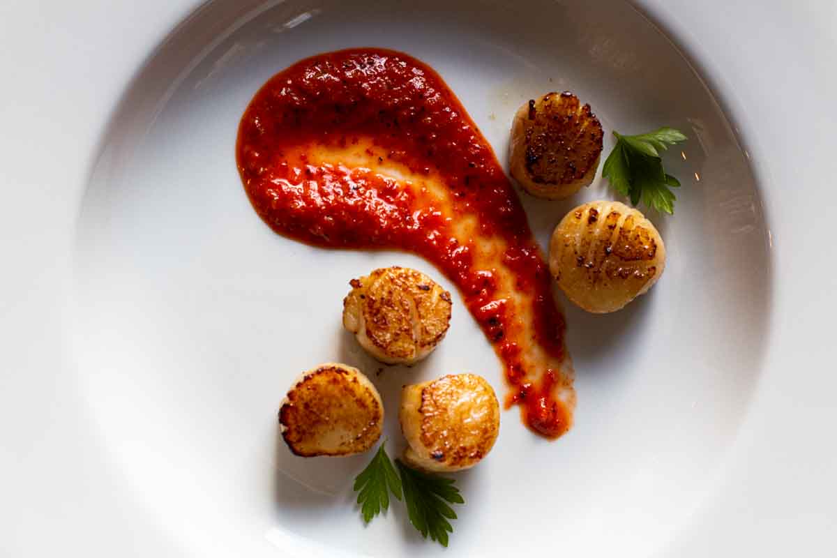 Red pepper coulis swirled on a plate and served with seared scallops.