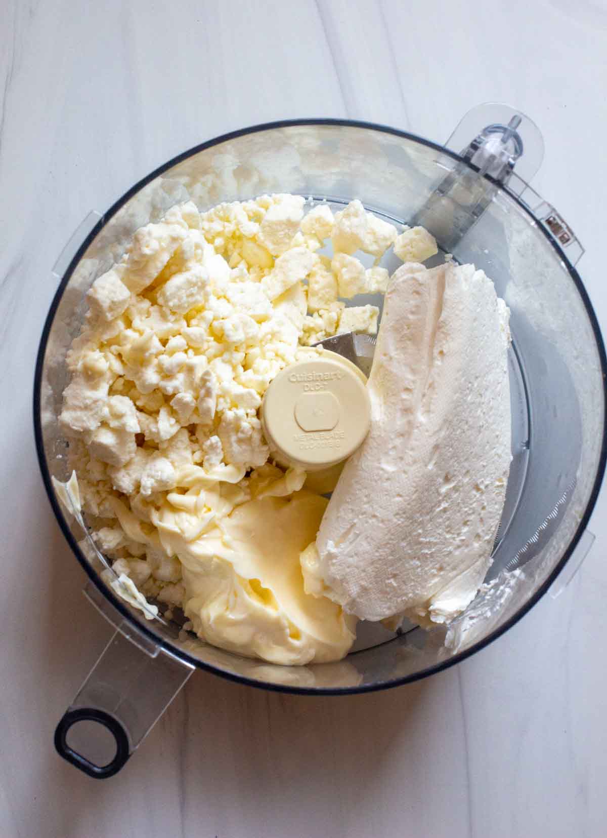 Blending feta cheese and cream cheese in a food processor.