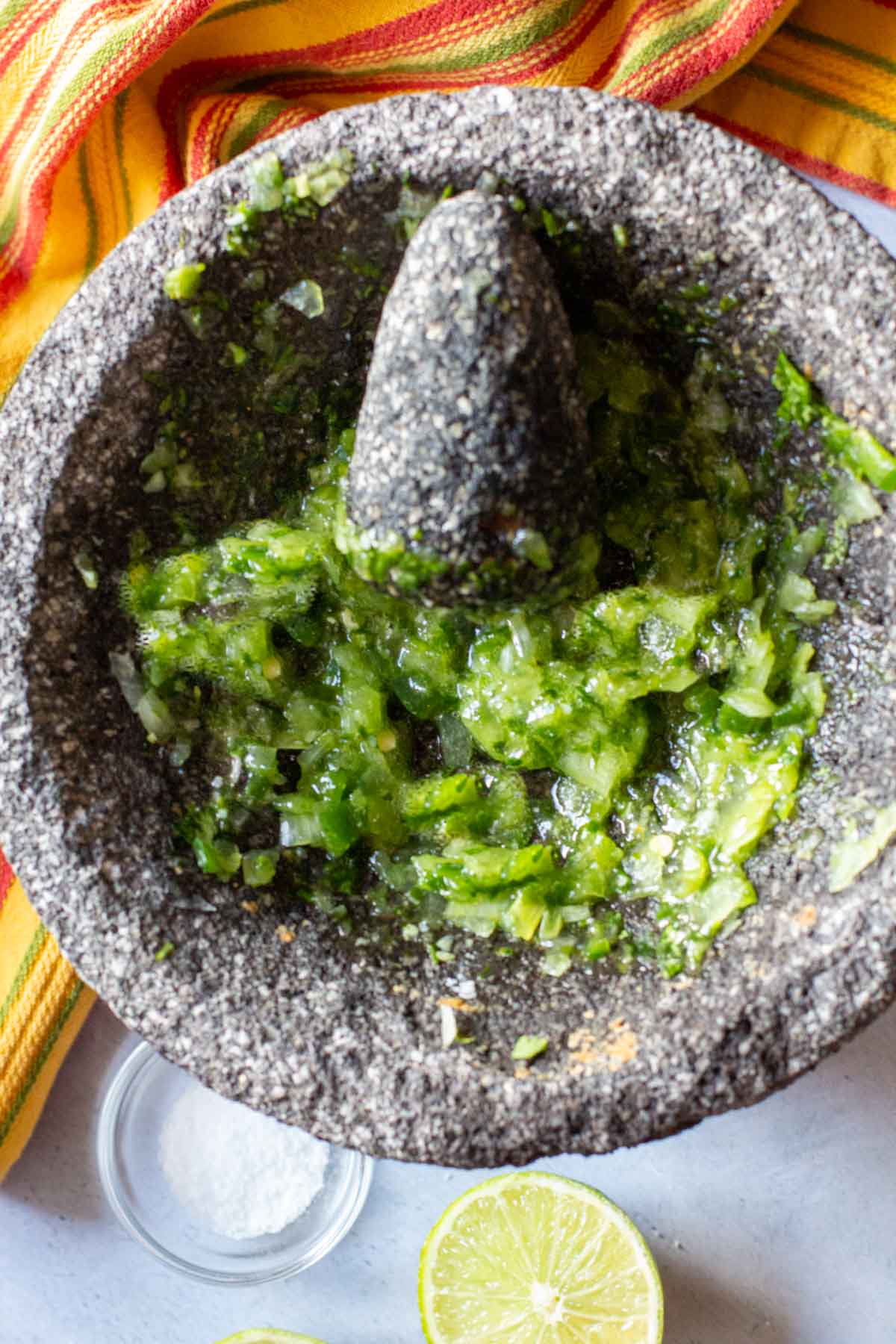Grinding vegetables and spices in a molcajete to make chunky guacamole.