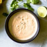 Homemade chipotle mayo in a bow surrounded by cilantro and lime.
