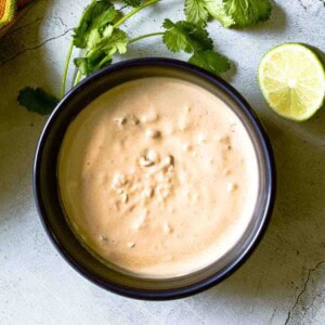 Homemade chipotle mayo in a bow surrounded by cilantro and lime.