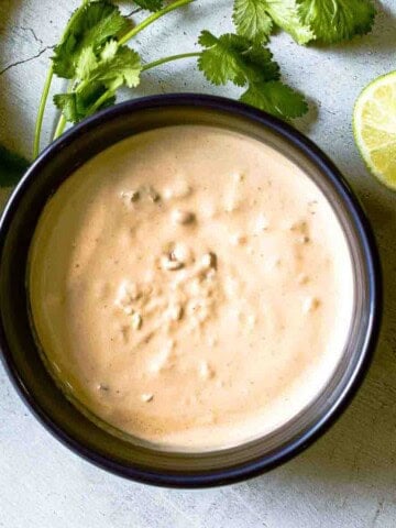 Homemade chipotle mayo in a bow surrounded by cilantro and lime.