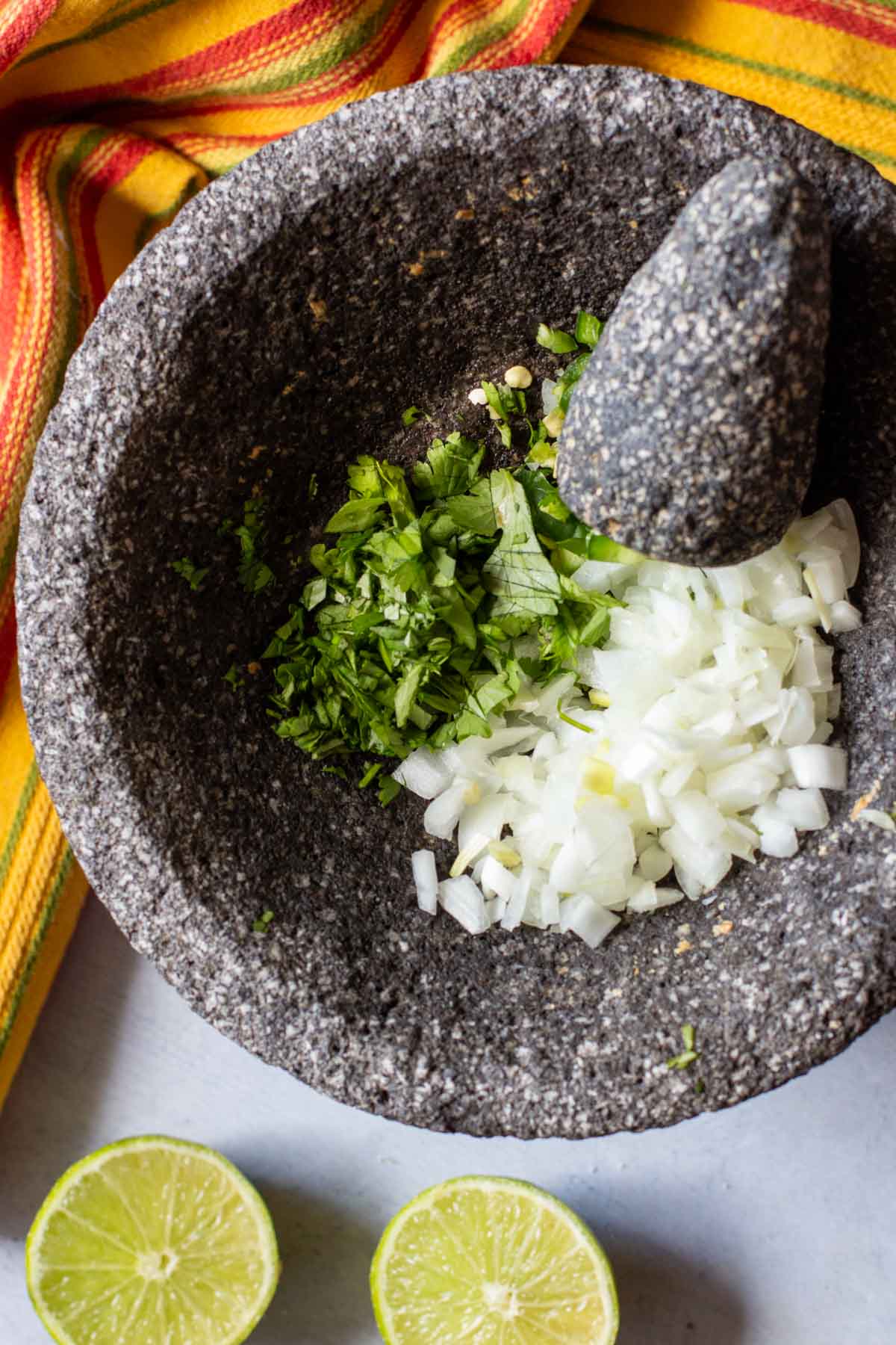 Adding vegetables to a molcajete to make chunky guacamole