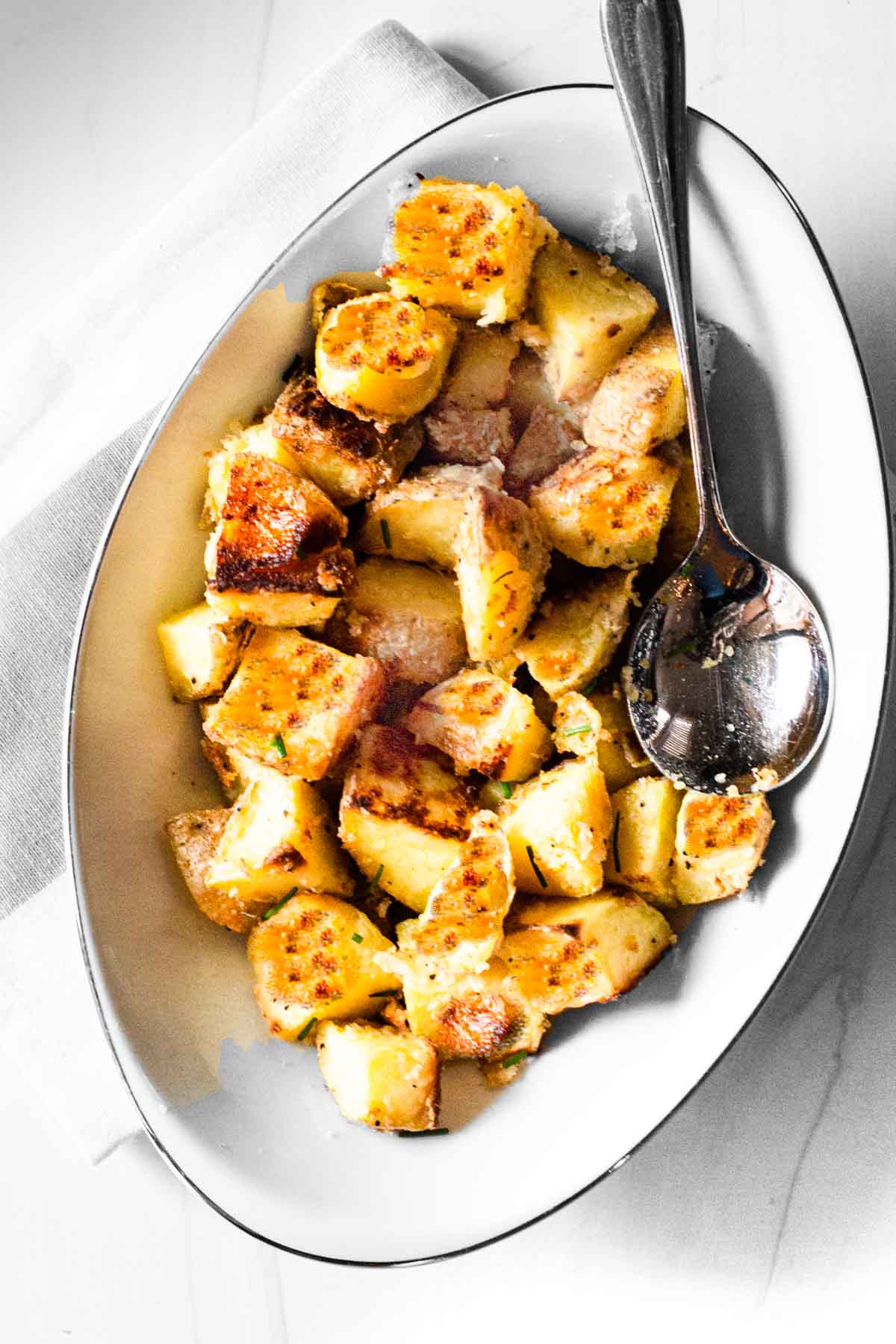 Parmesan crusted potatoes cubes in a white serving bowl.