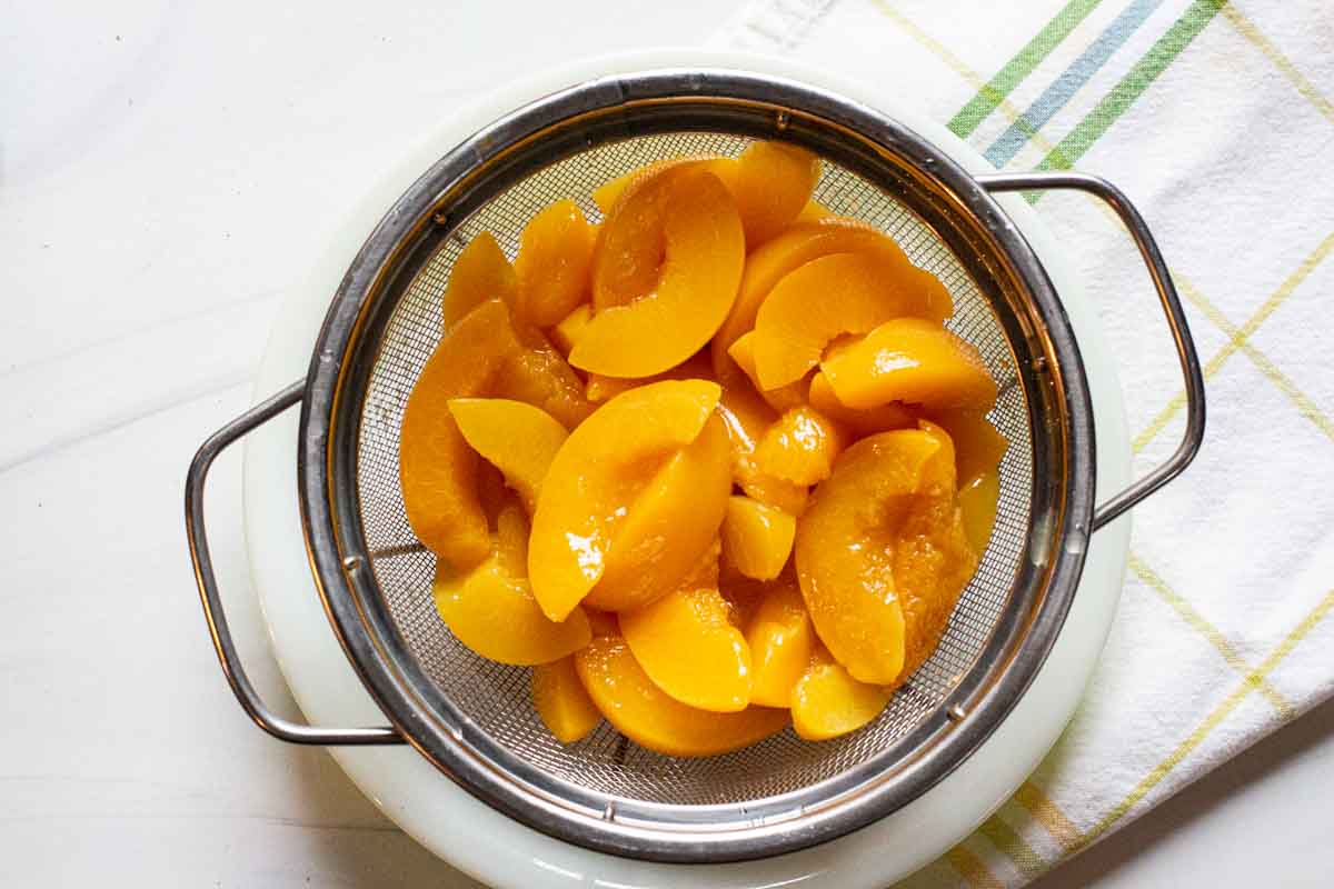 Draining canned peaches to make peach crumble pie.