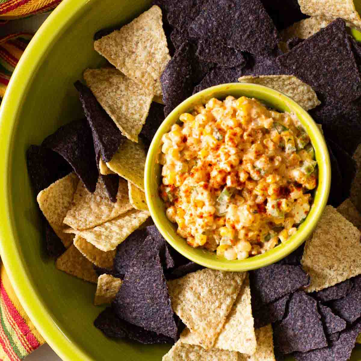 Mexican street corn dip served with blue and yellow corn tortillas.