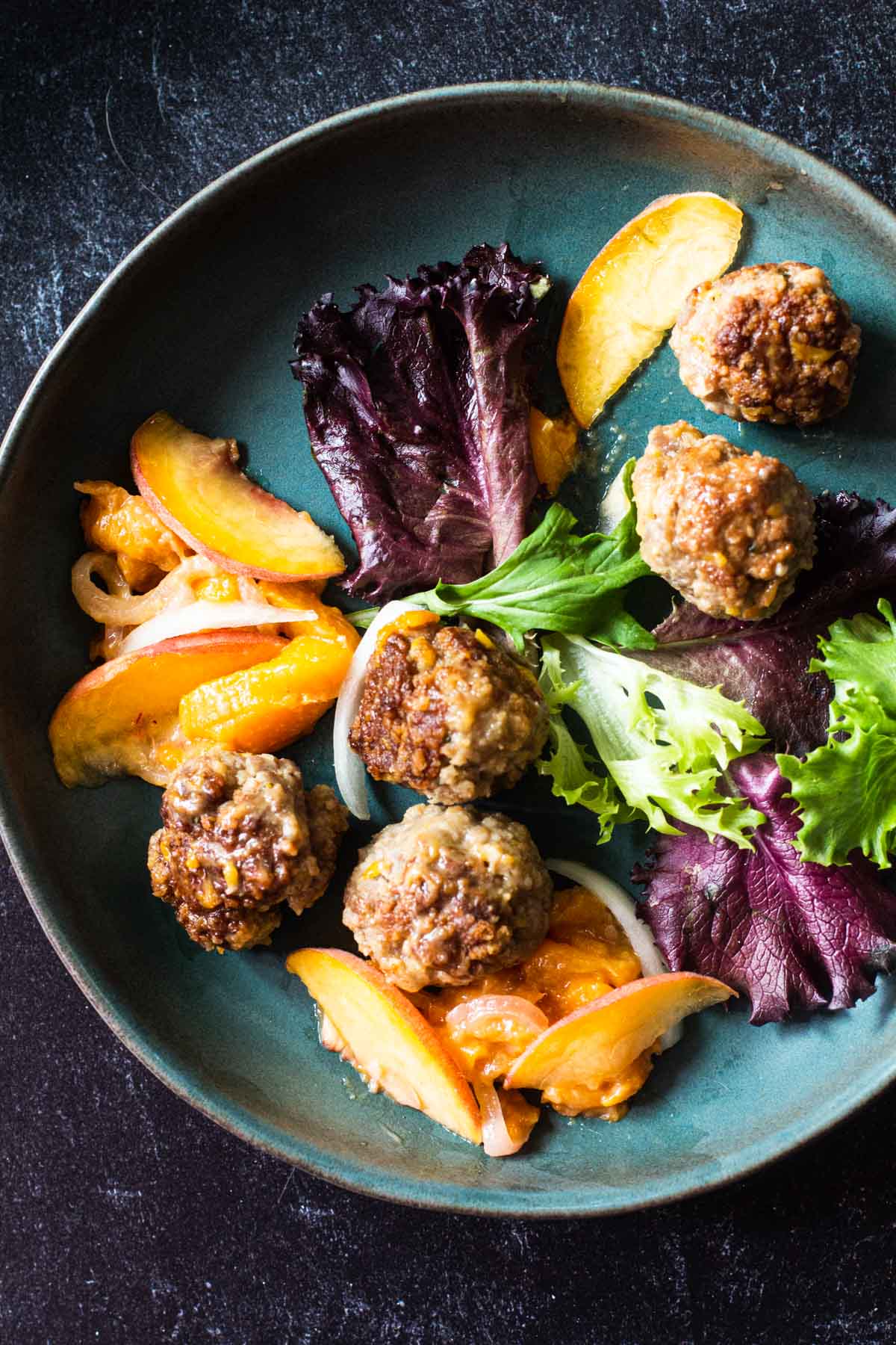 Pan fried meatballs with peaches served with mixed greens.