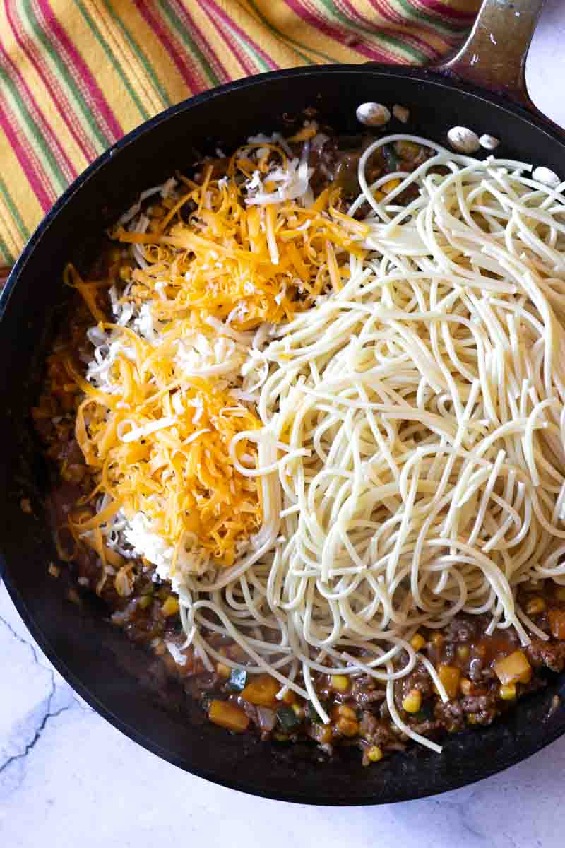 Adding cooked spaghetti and cheese to make cowboy spaghetti.