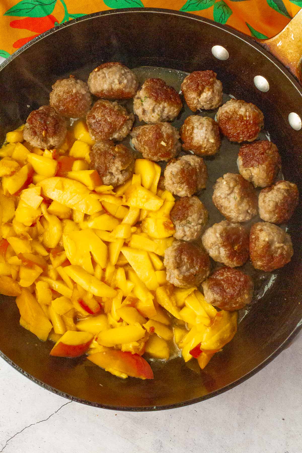 Frying pork meatballs in a skillet with peaches.