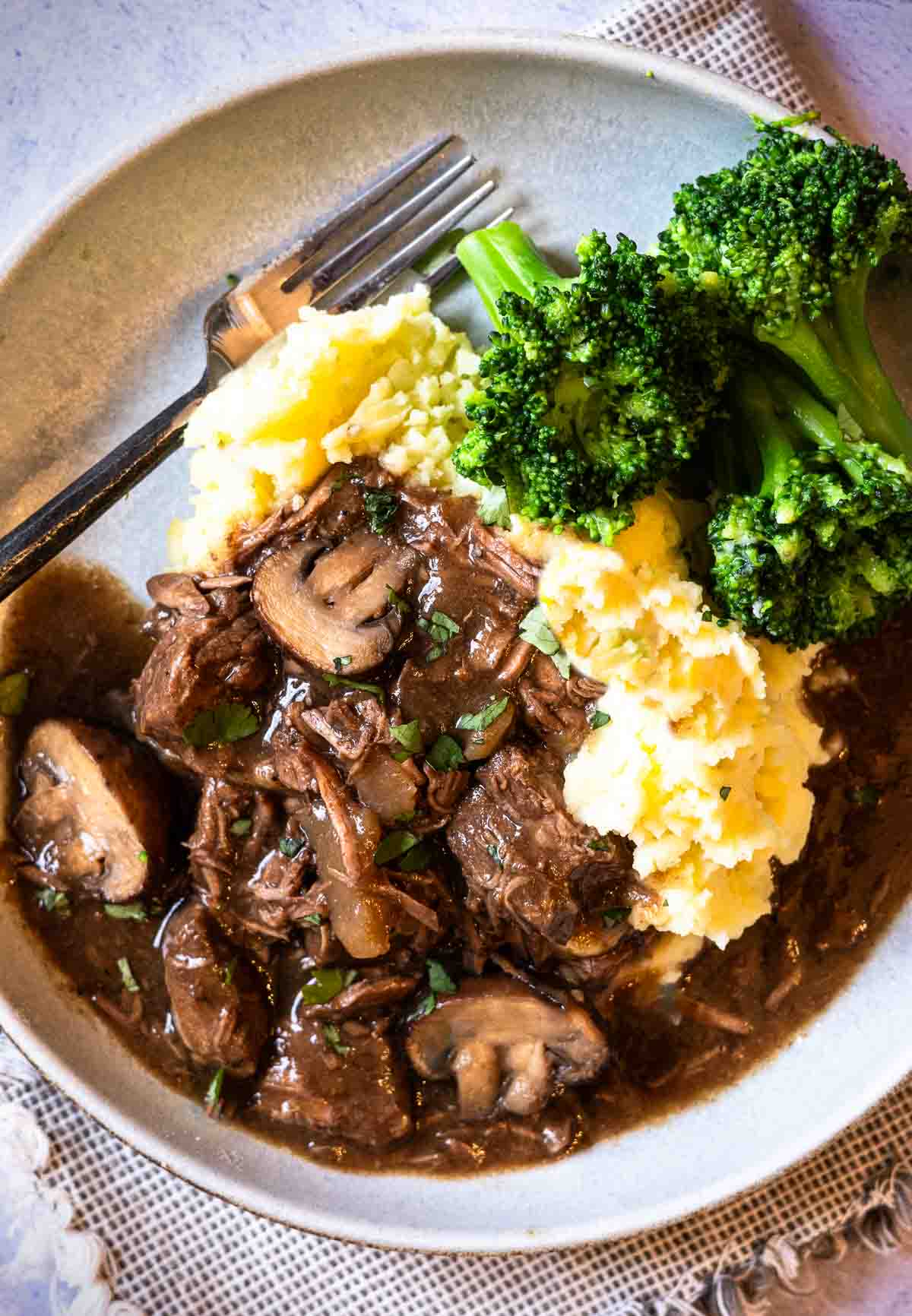 Slow cooker beef tips with gravy served with mashed potatoes and broccoli.