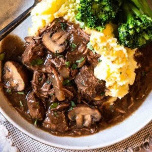 Slow cooker beef tips with gravy plated with mashed potatoes and broccoli.